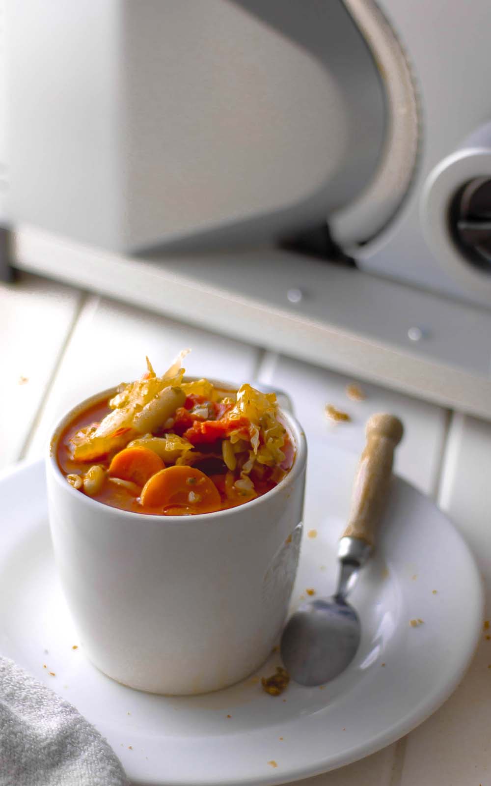 Weiße Tasse gefüllt mit bunter Kohlsuppe, mit Karottenscheiben, Tomatenstücken und frischem Kraut, serviert auf einem Teller mit Löffel. Weiße Tasse gefüllt mit bunter Kohlsuppe, mit Karottenscheiben, Tomatenstücken und frischem Kraut, serviert auf einem Teller mit Löffel.
