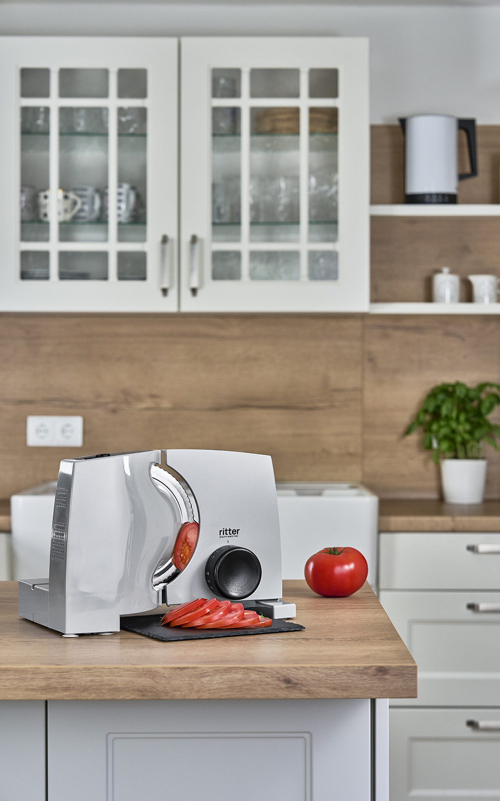 Ein Bild des elektrischen Allesschneiders, der auf einer Küchenplattform steht und Tomatenscheiben schneidet. Ein Bild des elektrischen Allesschneiders, der auf einer Küchenplattform steht und Tomatenscheiben schneidet.
