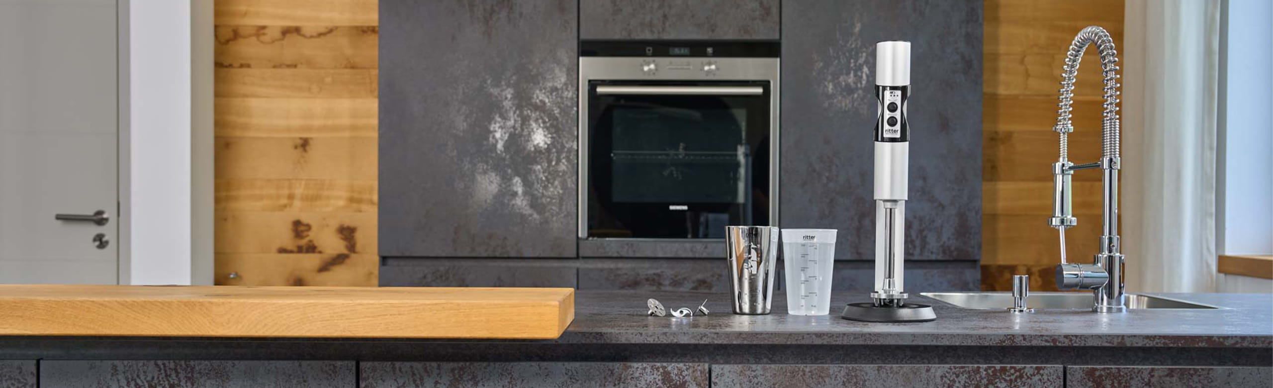 Ein Bild von einem silbernen Stabmixer und zwei Messbechern, die auf einer Küchenarbeitsplatte stehen.