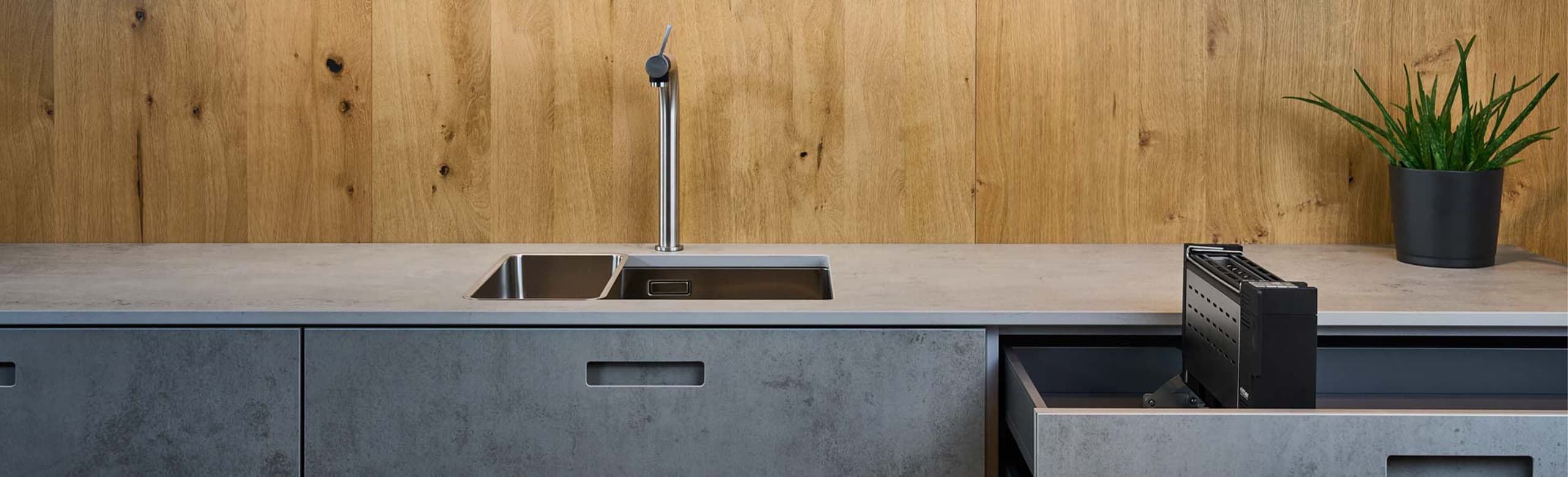 Ein Bild von einem Einbau-Toaster, der aus einer Küchenschublade hervorkommt, und einer Pflanze die auf der Arbeitsfläche steht.