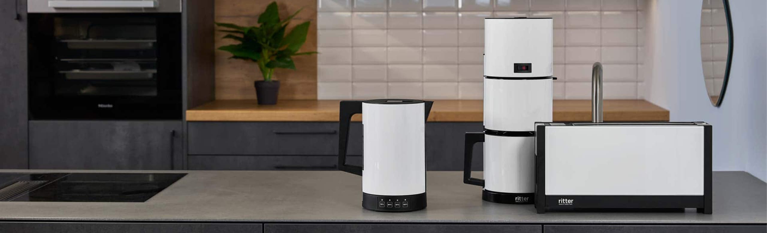 Ein Bild von einem weißen Toaster, Wasserkocher und einer Kaffeemaschine die neben einander auf einer Küchenplattform stehen.