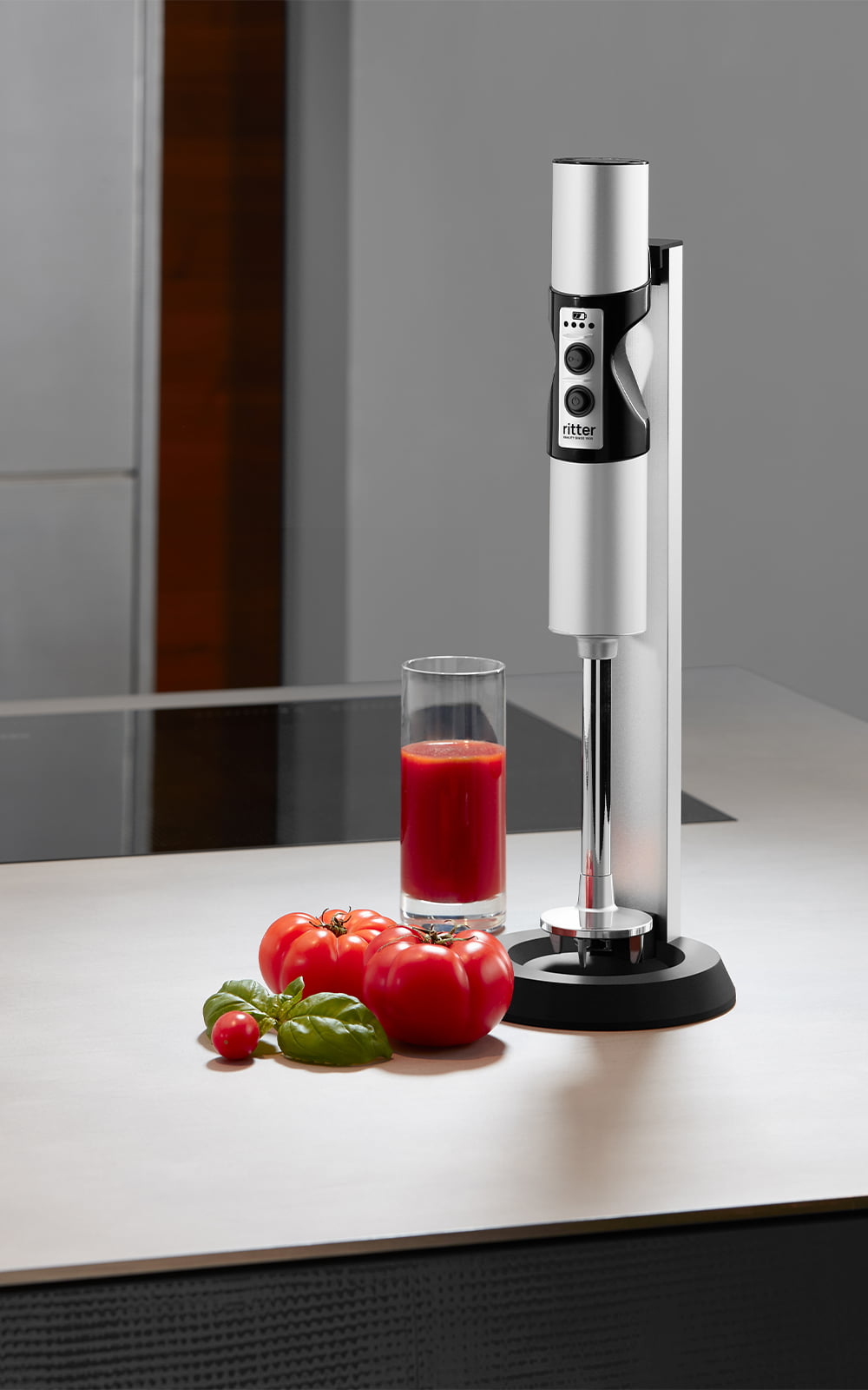 Ein Bild eines silbernen Stabmixers, der neben einem Glas Tomatensaft, in einer Küche steht. Ein Bild eines silbernen Stabmixers, der neben einem Glas Tomatensaft, in einer Küche steht.
