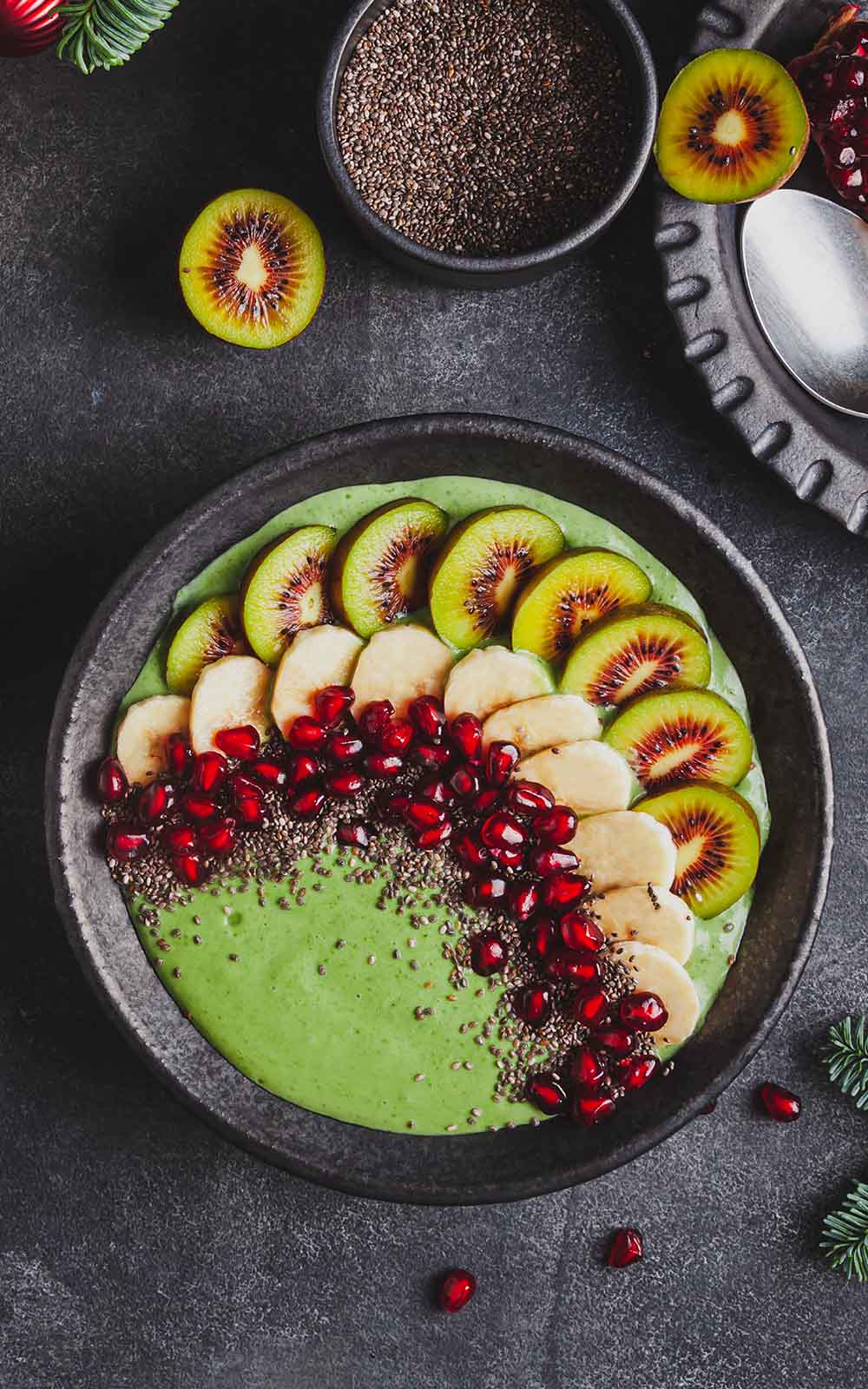 Grüne Smoothie Bowl, dekoriert mit Kiwi-Scheiben, Bananenscheiben, Granatapfelkernen und Chiasamen in einer schwarzen Schale. Grüne Smoothie Bowl, dekoriert mit Kiwi-Scheiben, Bananenscheiben, Granatapfelkernen und Chiasamen in einer schwarzen Schale.