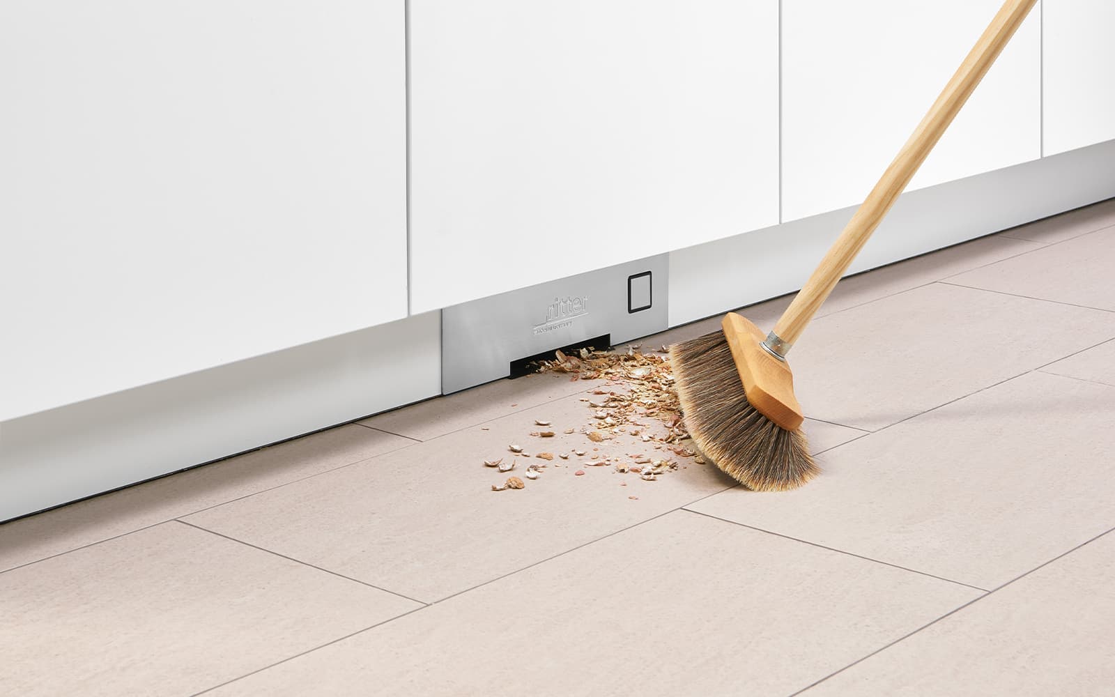 Einen Besen der Krümel zum Einbau-Sockelsauger fegt.