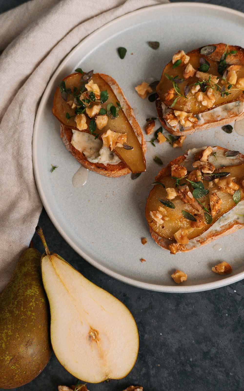 Knusprige Crostini mit cremigem Belag, karamellisierter Birne, Walnüssen und frischen Kräutern, serviert auf einem hellen Teller