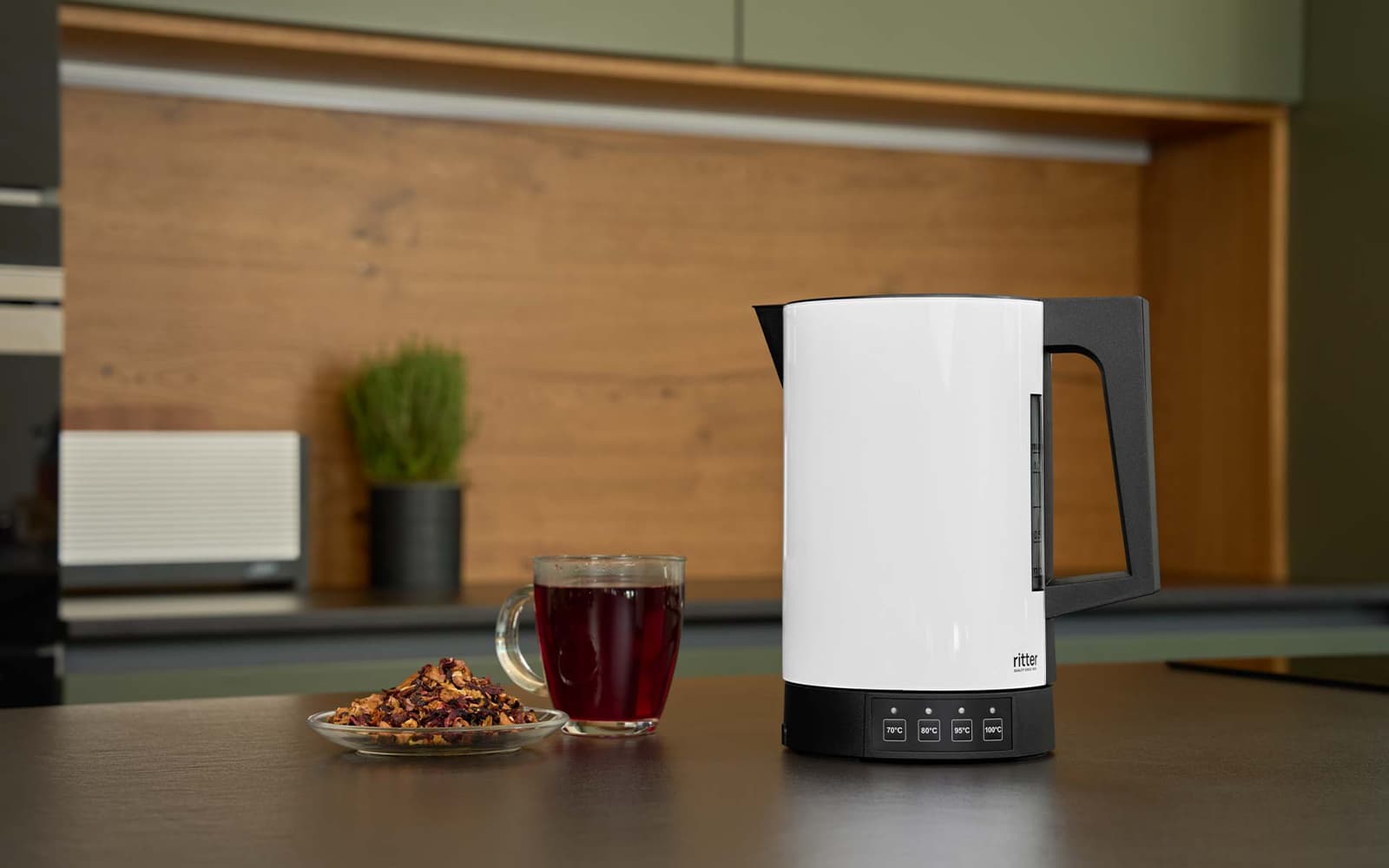 Ein Bild des weißen Wasserkochers, der auf einer Küchenplattform, neben einer Tasse Tee, steht.