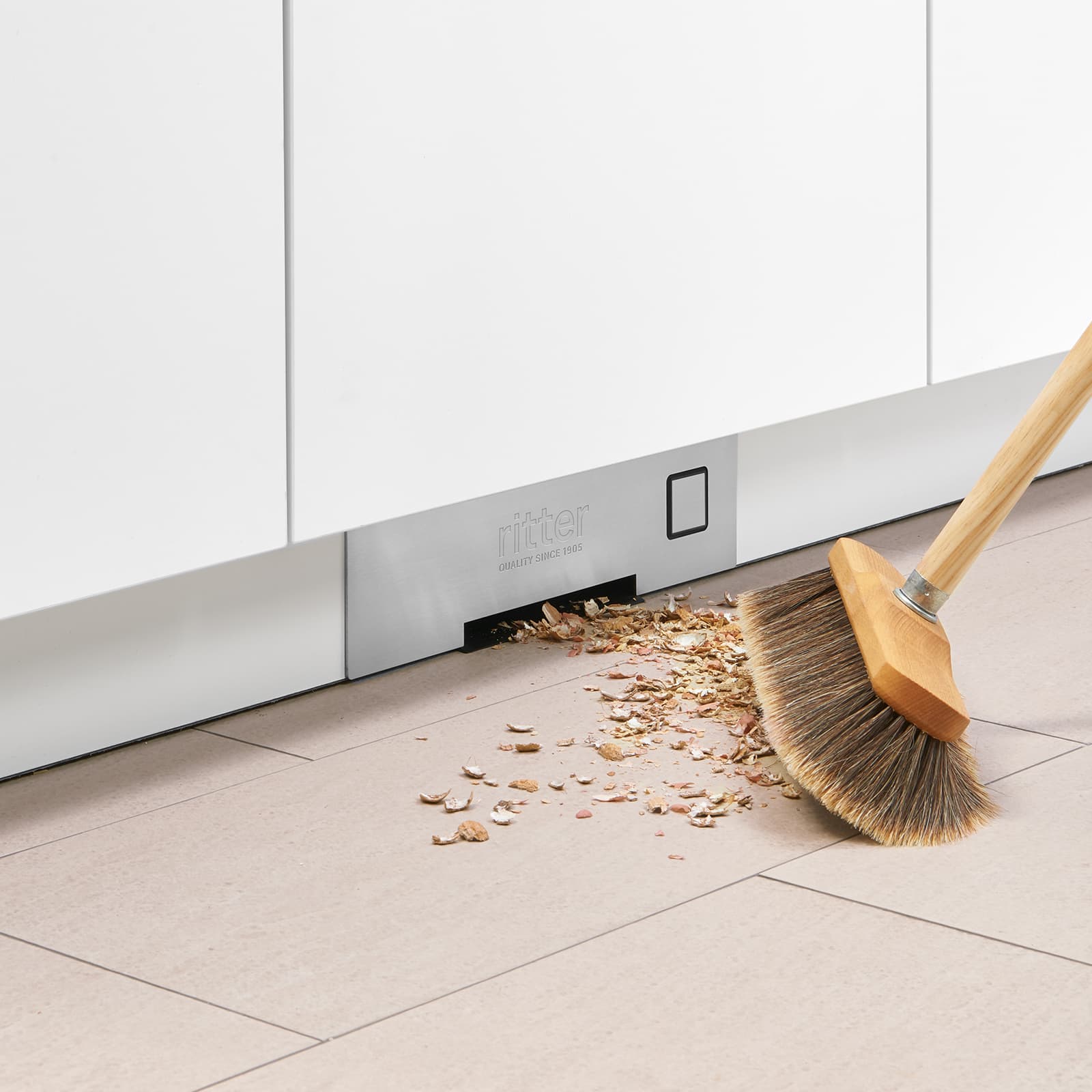 Ein Bild von einem Besen, der Krümel zum Einbau-Sockelsauger fegt.