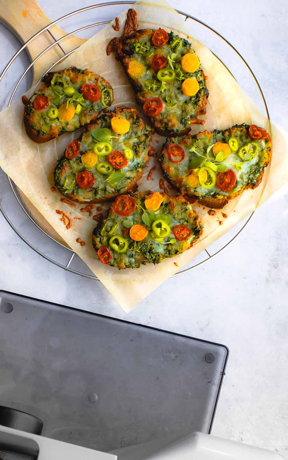 Ofengebackene Brotscheiben mit geschmolzenem Käse, buntem Gemüse-Topping aus Tomaten, Paprika und frischen Kräutern, serviert auf Backpapier