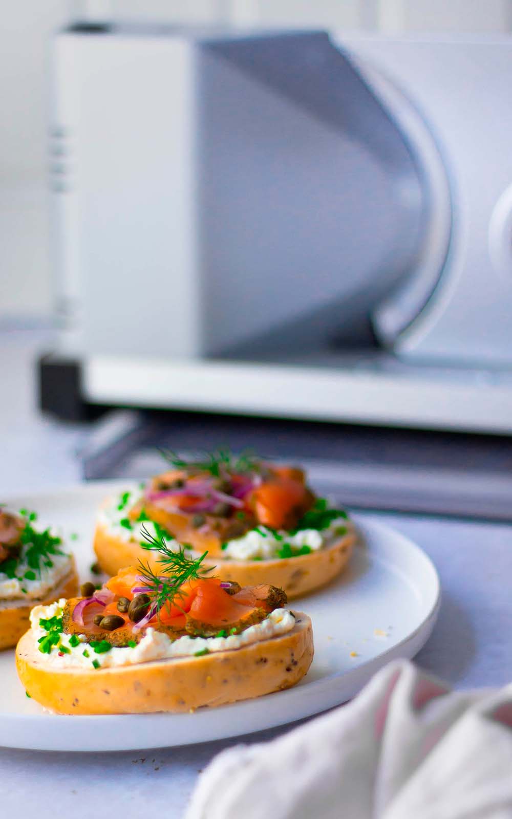 Frischer Bagel mit Frischkäse, Räucherlachs, roten Zwiebeln, Kapern und Kräutern, serviert auf einem weißen Teller. Frischer Bagel mit Frischkäse, Räucherlachs, roten Zwiebeln, Kapern und Kräutern, serviert auf einem weißen Teller.