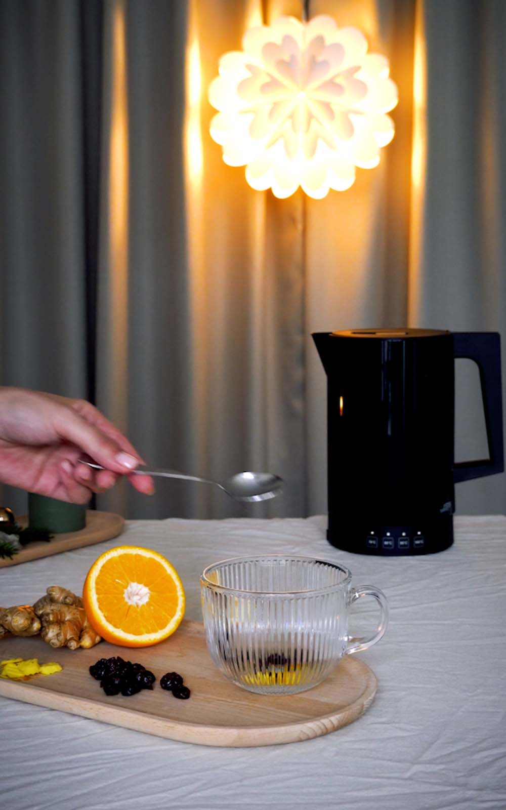 Zubereitung einer Cranberry-Ingwer-Infusion: Glas-Tasse auf Holzbrett mit getrockneten Cranberrys und Ingwerstücken darin, daneben frische Ingwerwurzel und halbierte Orange, im Hintergrund Wasserkocher und weihnachtliche Beleuchtung. Zubereitung einer Cranberry-Ingwer-Infusion: Glas-Tasse auf Holzbrett mit getrockneten Cranberrys und Ingwerstücken darin, daneben frische Ingwerwurzel und halbierte Orange, im Hintergrund Wasserkocher und weihnachtliche Beleuchtung.