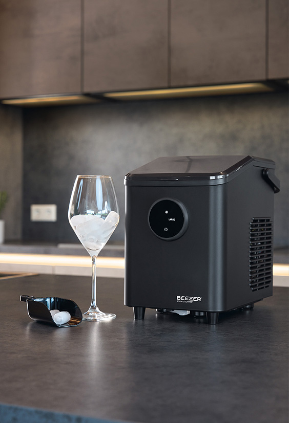 Schwarze Eiswürfelmaschine daneben Glas mit Eiswürfel gefüllt.