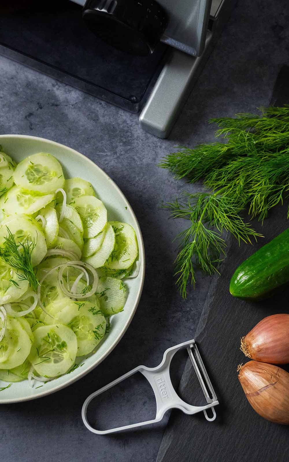 Frischer Gurkensalat mit dünn geschnittenen Gurken, Zwiebelringen und Dill in einer Schale, daneben frische Zutaten wie Gurke, Schalotten und Dill. Frischer Gurkensalat mit dünn geschnittenen Gurken, Zwiebelringen und Dill in einer Schale, daneben frische Zutaten wie Gurke, Schalotten und Dill.