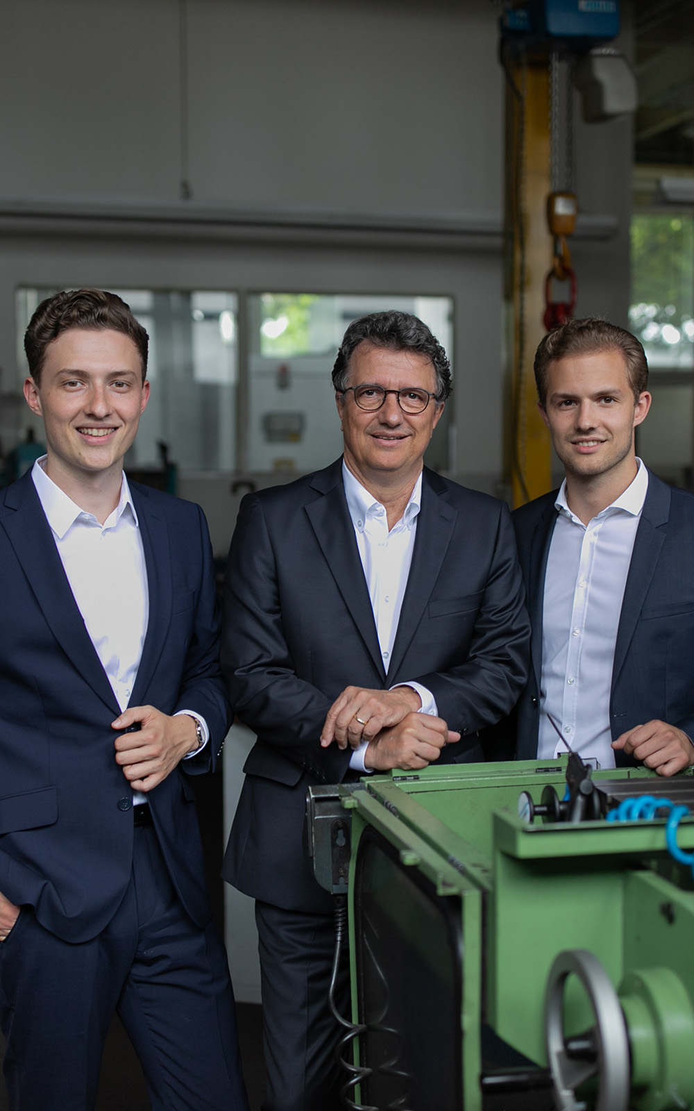 Ein Bild von drei Männern mit Anzügen, die in einer Werkstatt stehen und in die Kamera lächeln. Ein Bild von drei Männern mit Anzügen, die in einer Werkstatt stehen und in die Kamera lächeln.