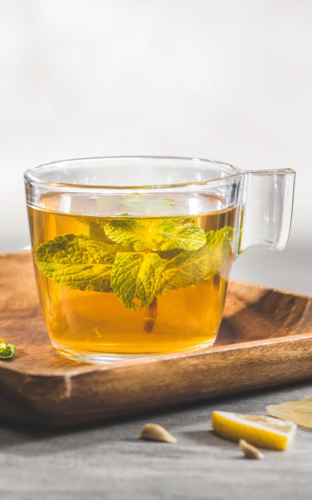 Glas mit heißem Kräutertee, darin frische Minzblätter, auf einem Holztablett mit Zitronenscheibe und Kernen. Glas mit heißem Kräutertee, darin frische Minzblätter, auf einem Holztablett mit Zitronenscheibe und Kernen.