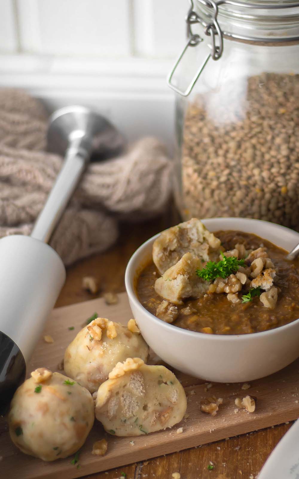 Schüssel mit Walnuss-Linsen-Eintopf, garniert mit frischen Kräutern und Walnüssen, daneben hausgemachte Knödel auf einem Holzbrett. Schüssel mit Walnuss-Linsen-Eintopf, garniert mit frischen Kräutern und Walnüssen, daneben hausgemachte Knödel auf einem Holzbrett.