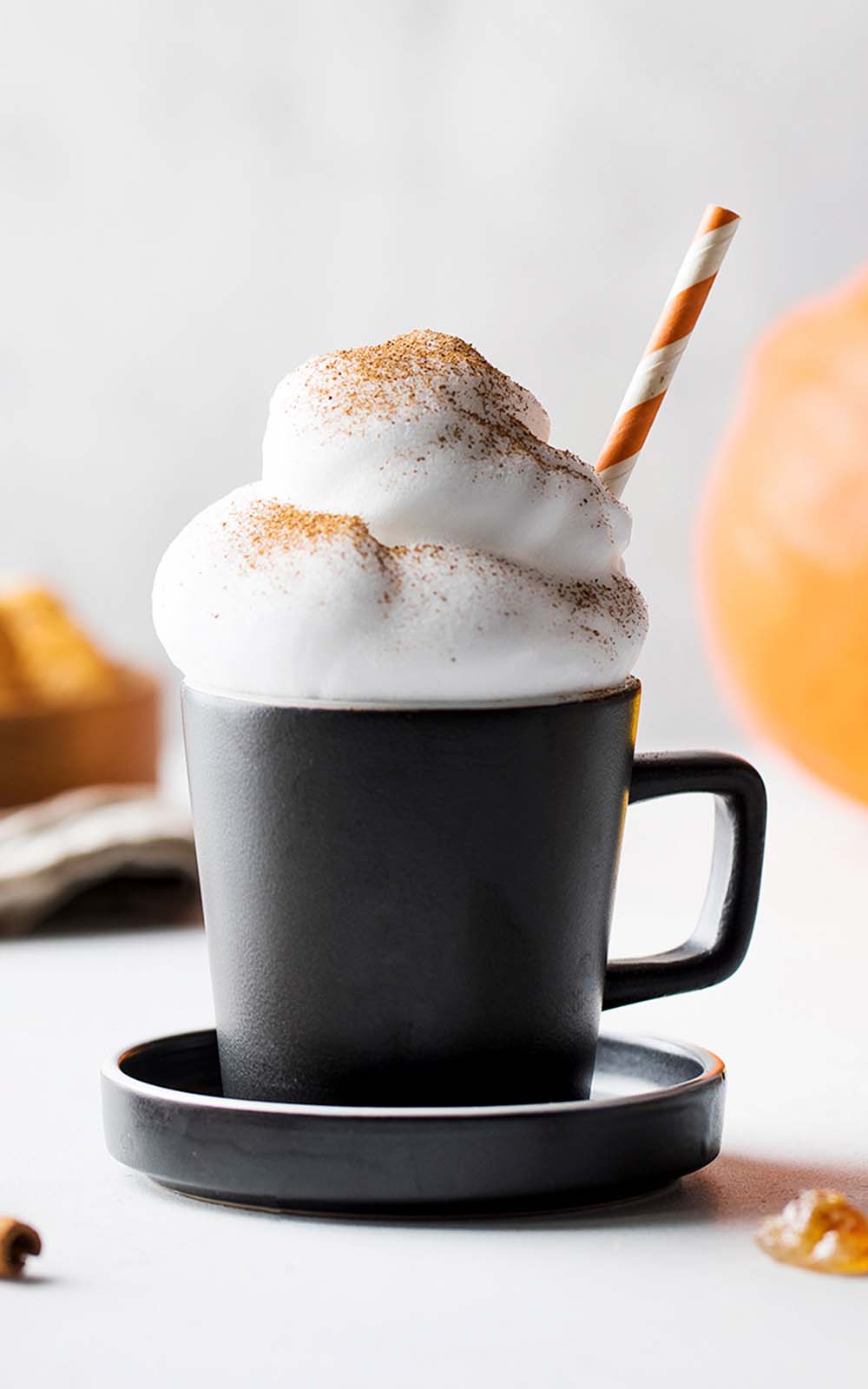 Schwarze Tasse mit Pumpkin Spice Latte, getoppt mit viel Milchschaum, bestäubt mit Zimt, dazu ein gestreifter Strohhalm. Schwarze Tasse mit Pumpkin Spice Latte, getoppt mit viel Milchschaum, bestäubt mit Zimt, dazu ein gestreifter Strohhalm.