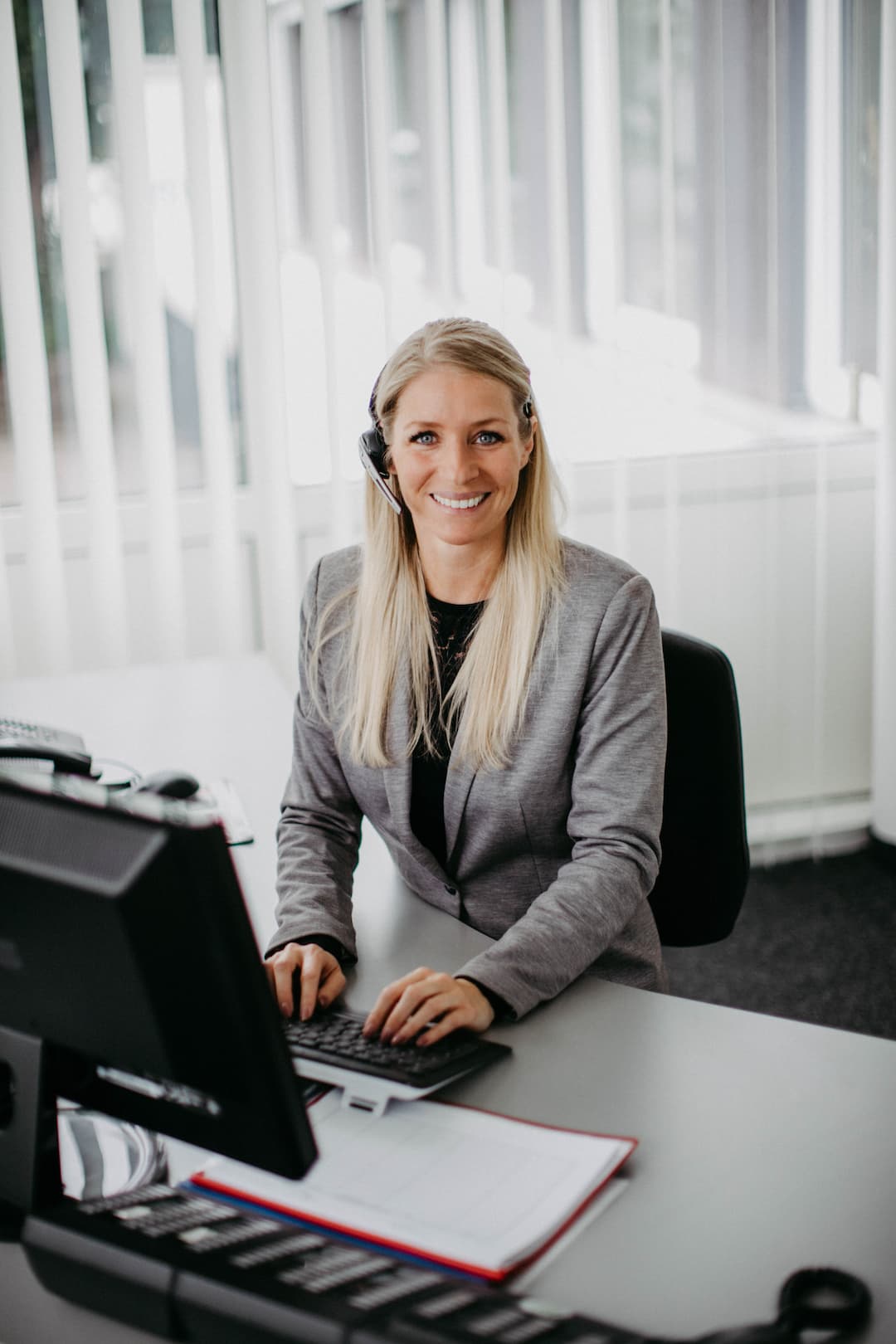 Ein Bild von einer blonden Frau, die mit einem Headset am Computer sitzt und lacht. Ein Bild von einer blonden Frau, die mit einem Headset am Computer sitzt und lacht.