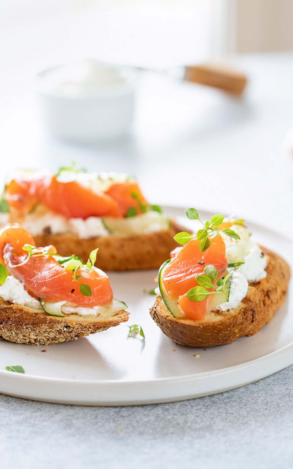 Knusprige Brotscheiben, belegt mit cremigem Frischkäse, Gurkenscheiben und geräuchertem Lachs, garniert mit frischen Kräutern, auf einem weißen Teller angerichtet. Knusprige Brotscheiben, belegt mit cremigem Frischkäse, Gurkenscheiben und geräuchertem Lachs, garniert mit frischen Kräutern, auf einem weißen Teller angerichtet.